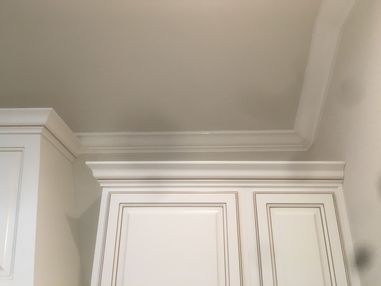 White kitchen cabinets with decorative crown molding meeting a beige ceiling