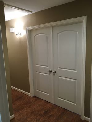 White double closet doors in a dim hallway with brown walls and wood flooring.