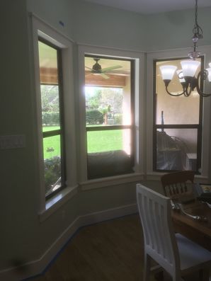Bright bay window nook with chair and chandelier, overlooking a green yard.