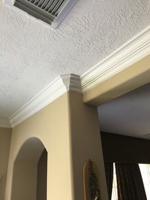 Interior corner with textured white ceiling, crown molding, beige wall, and a ceiling vent above an arched doorway