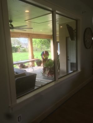 View through a window into a screened porch with a person sitting at a table and a green lawn beyond