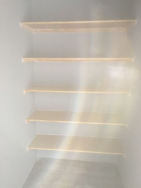 Empty walk-in closet with five light wood shelves and a hanging rod on the right wall