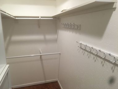 Empty white walk-in closet with shelves, hanging rods, and a row of hooks along the right wall.