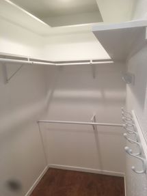 Empty white walk-in closet with hanging rods, shelves, and a wooden floor.