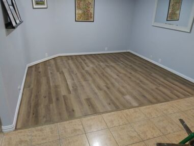 Empty room with gray walls, tan tile and wood flooring, and framed wall art.
