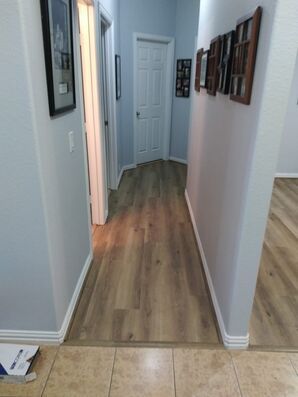 Hallway with wood flooring, white doors, and framed photos on the wall, viewed from a tiled entryway
