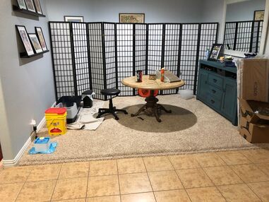 Home office with folding privacy screens, round table, chair, cabinet, and boxes on a tiled floor.