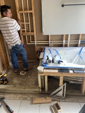 Worker standing in an unfinished room beside a protected bathtub and exposed wall framing