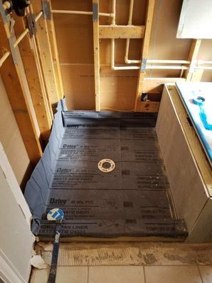 Unfinished bathroom with exposed wall studs, black subflooring, and a partially installed shower area