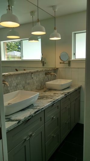 Bright bathroom with double sinks, marble countertop, green cabinets, and round pendant lights.