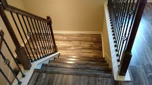 Top-down view of a wooden staircase with dark railings and beige walls, leading to a lower floor.
