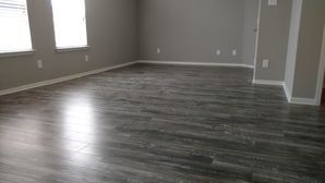 Empty room with gray wood flooring, beige walls, and two windows letting in natural light