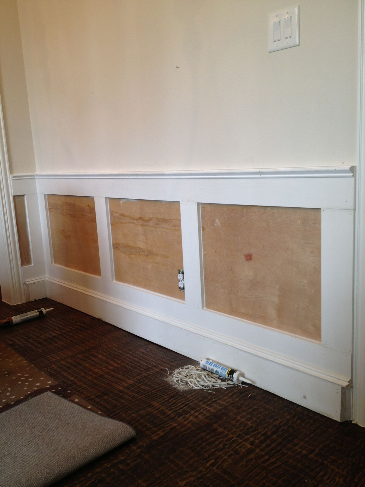 Bare wall with white wainscoting and three covered openings above a carpeted floor