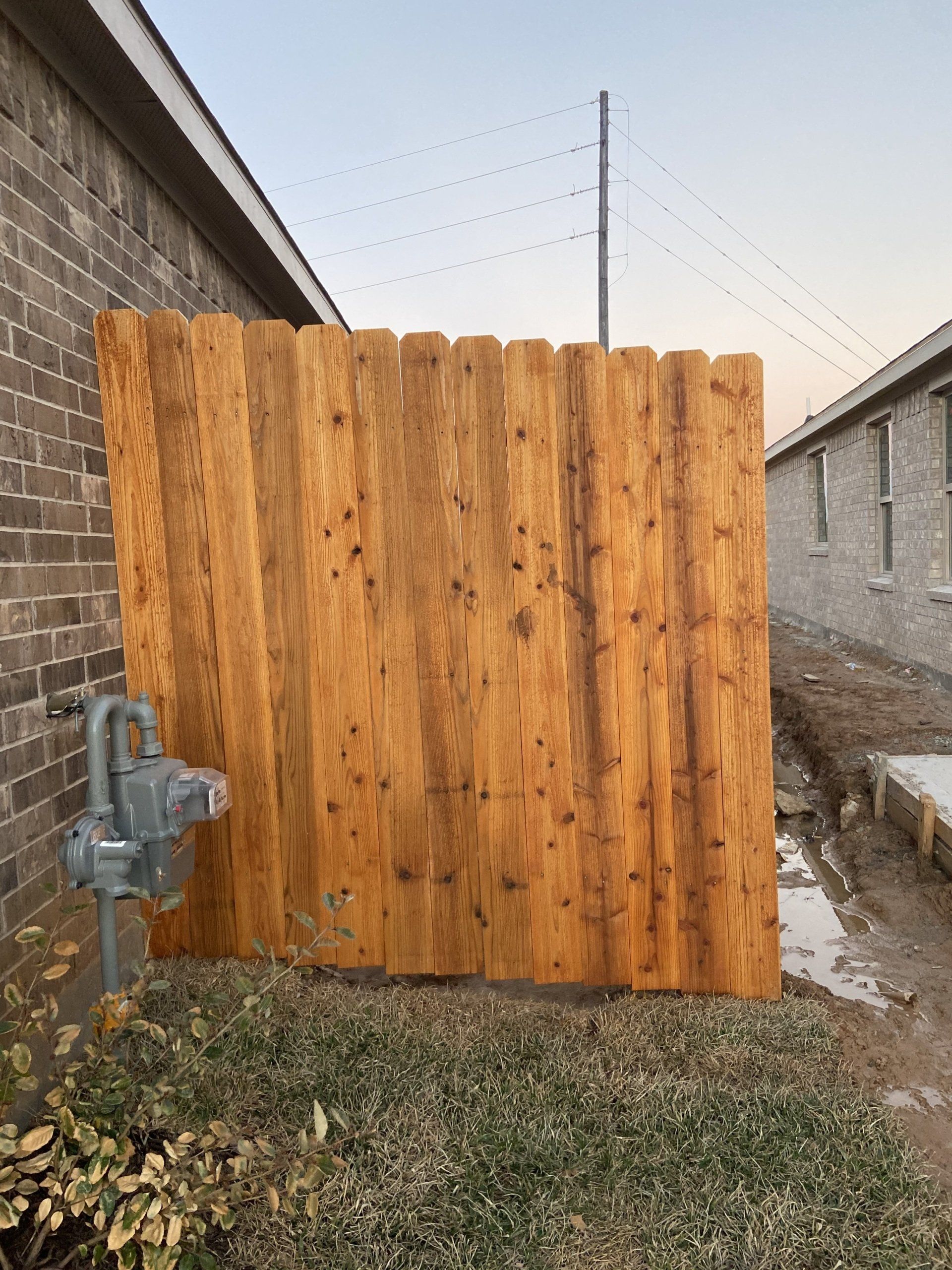 Wooden privacy fence gate between two brick walls in a narrow side yard.