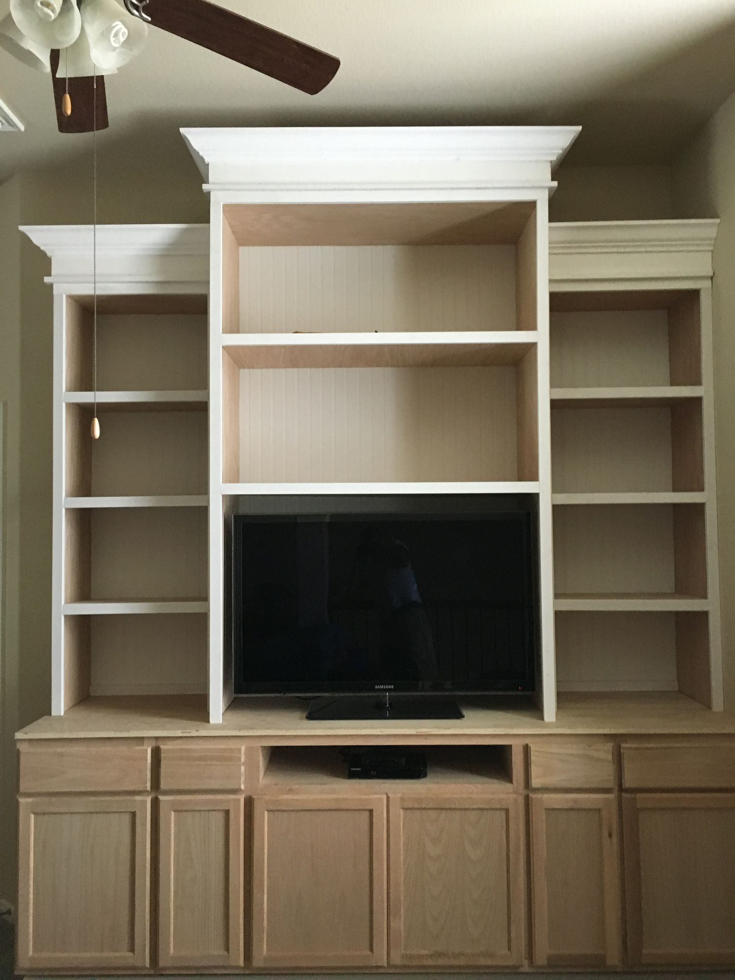 Built-in beige entertainment center with shelves, cabinets, and a TV in the middle, in a living room.
