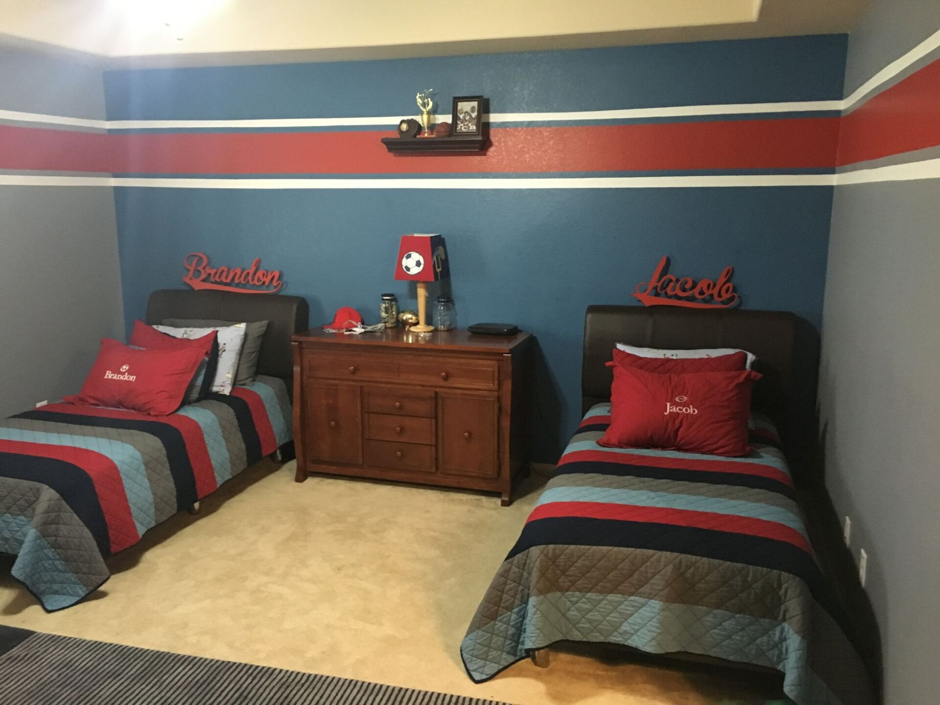 Two twin beds with red, white, and blue bedding flank a wooden dresser in a blue bedroom.