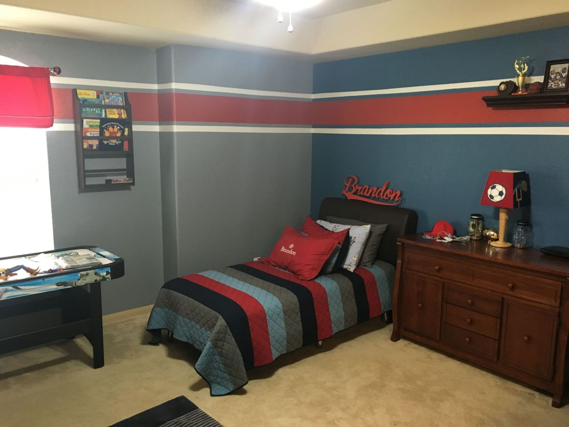Teen bedroom with gray walls, red and blue striped bedding, dresser, and dartboard-themed decor.