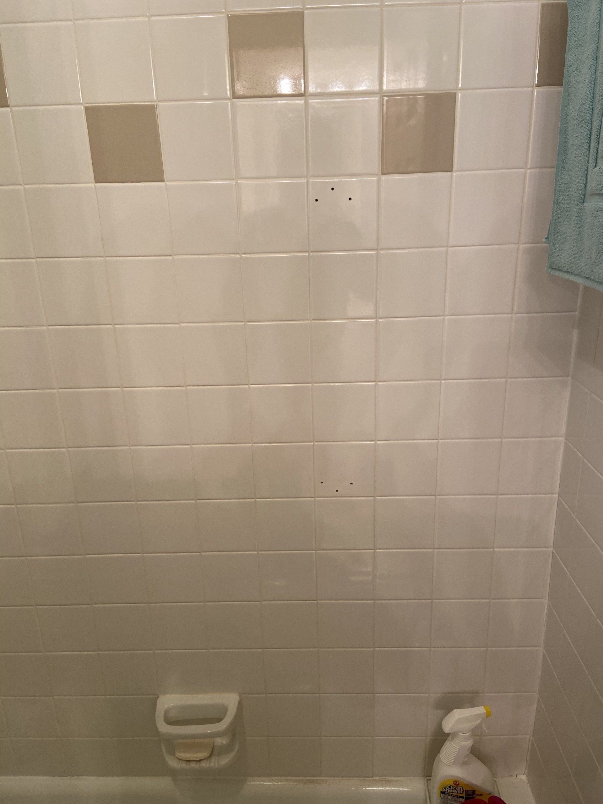 White tiled bathroom wall with a soap dish and a bottle on the floor near the shower area.