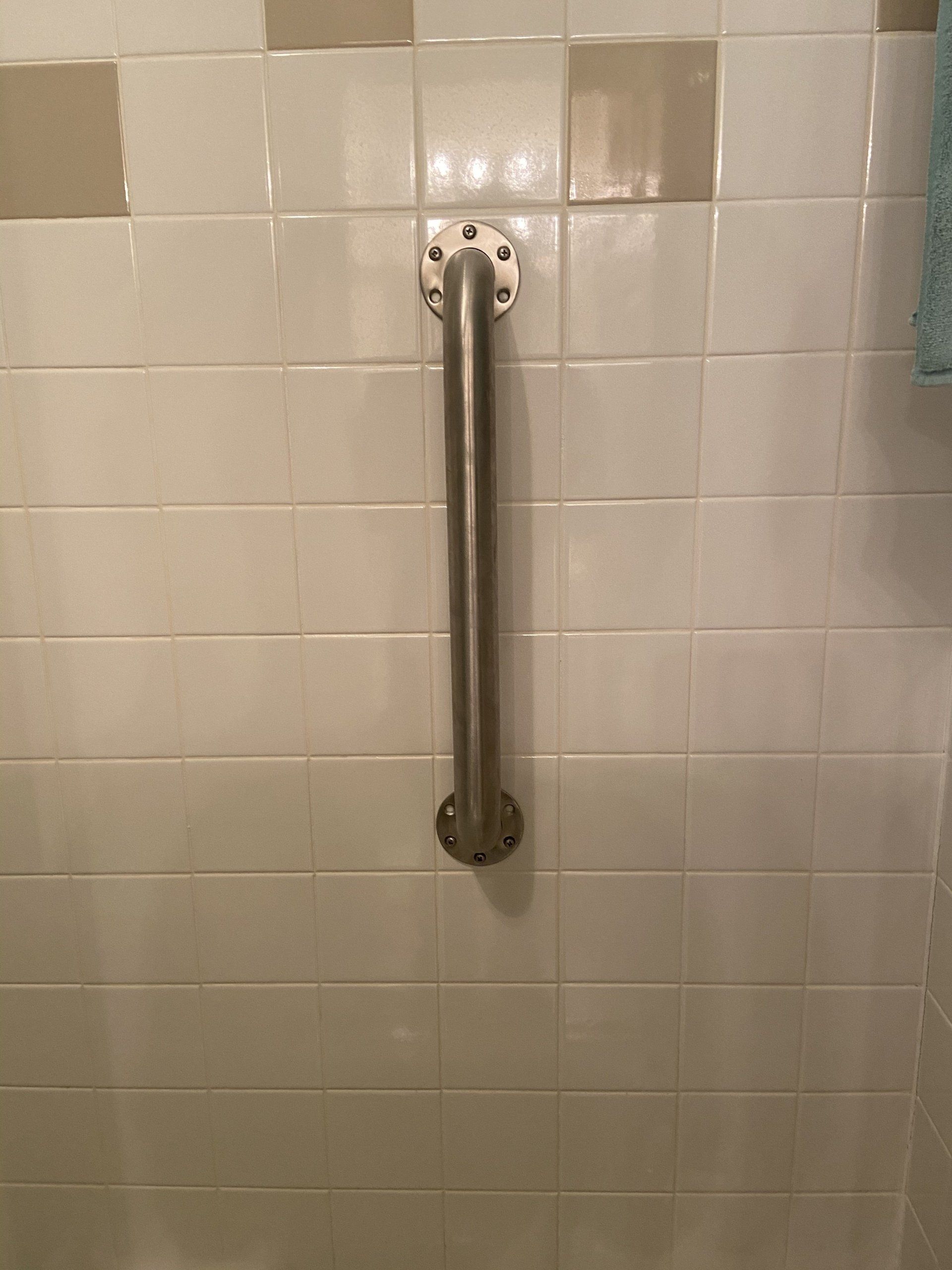 Vertical metal grab bar mounted on white tiled bathroom wall