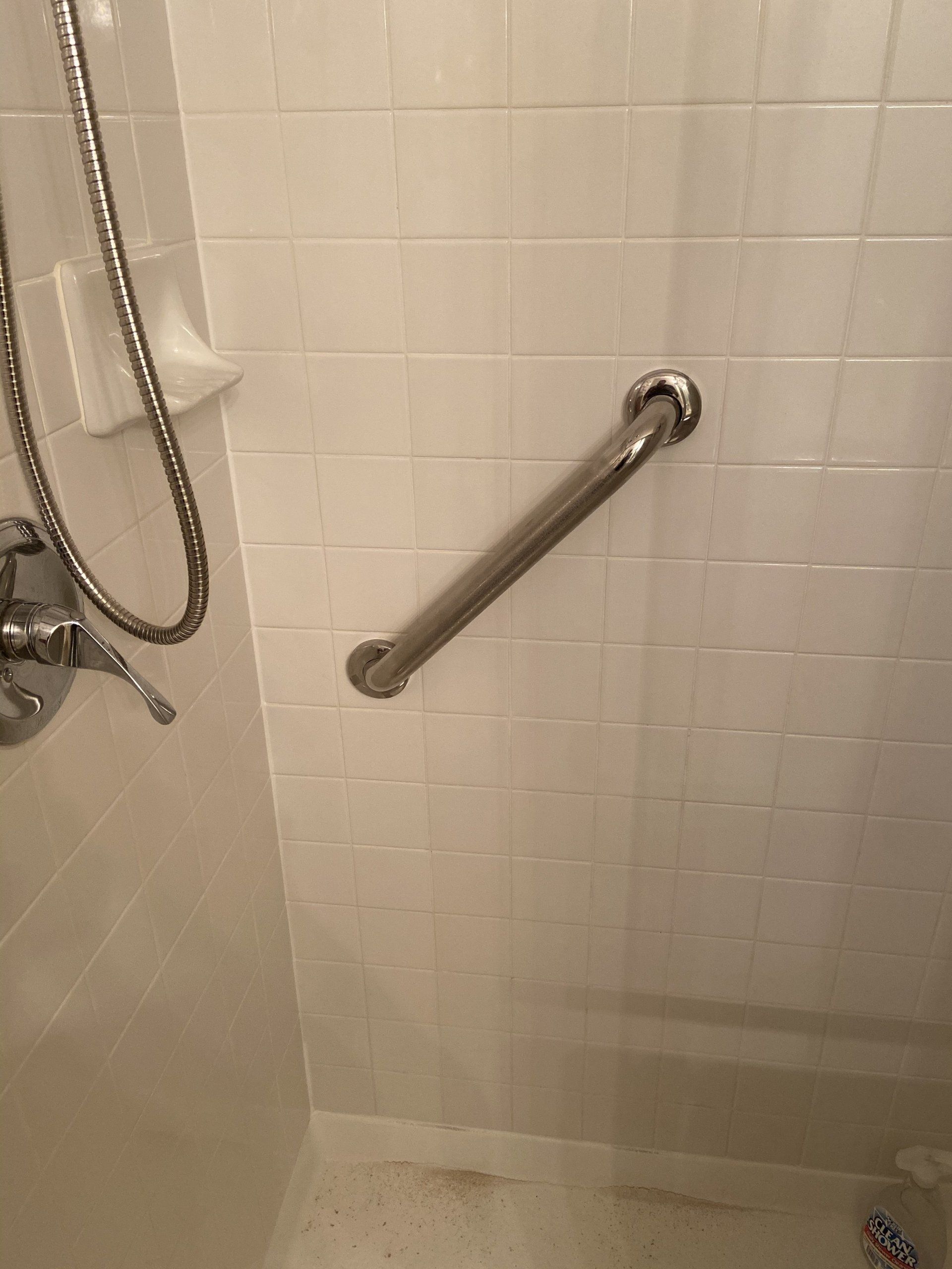 Shower stall with white tile walls, handheld showerhead, and a diagonal grab bar.