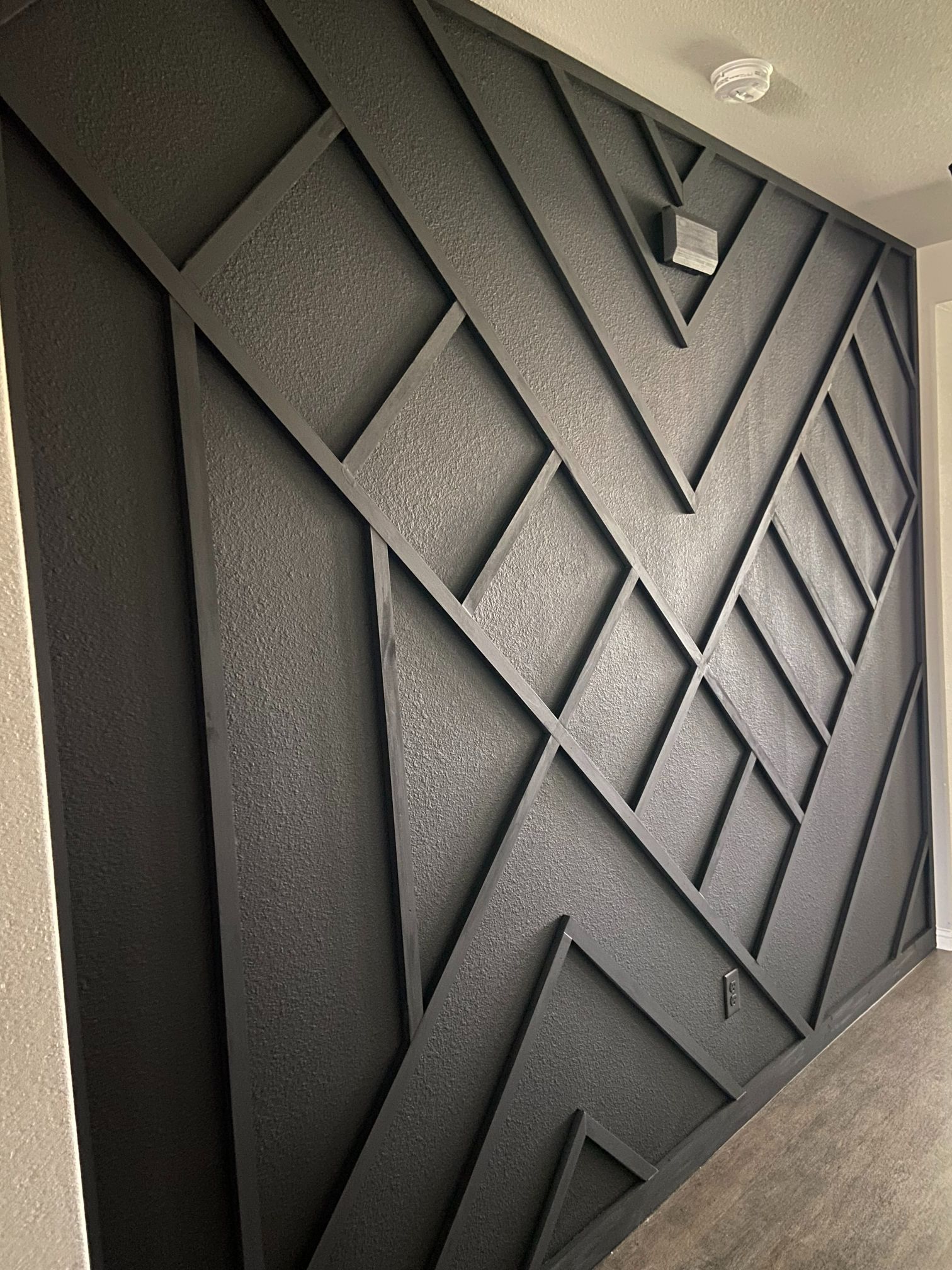 Gray geometric 3D wall panel with layered diamond and triangular patterns in a modern interior