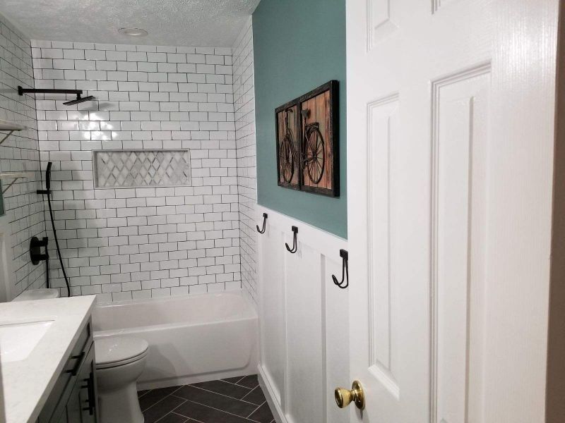 Small white bathroom with tub, subway tile shower, vanity, and framed wall art.