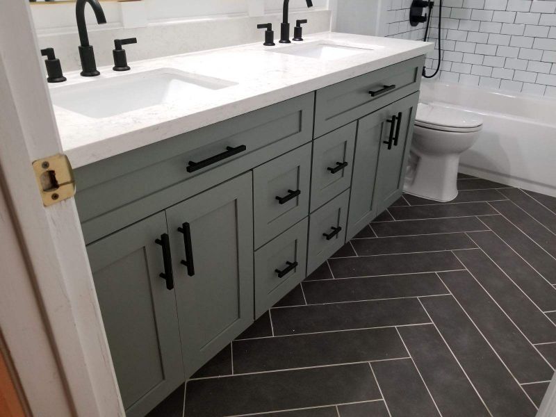 Modern bathroom with sage green vanity, white countertop, black fixtures, and gray herringbone tile floor
