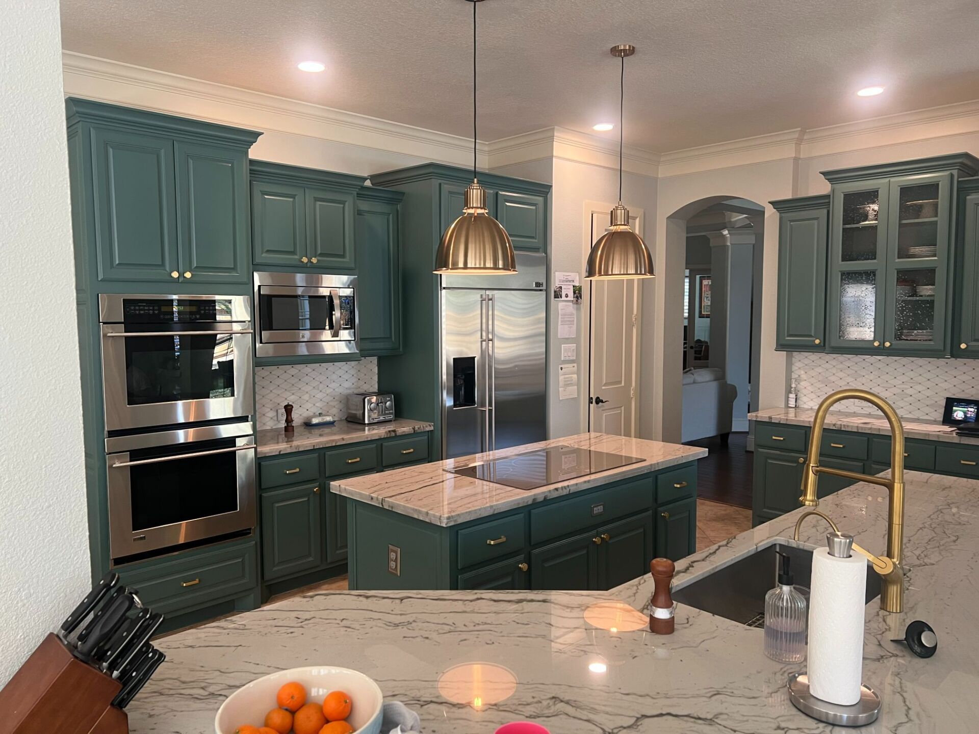 Elegant green kitchen with a large island, stainless steel appliances, and gold pendant lights