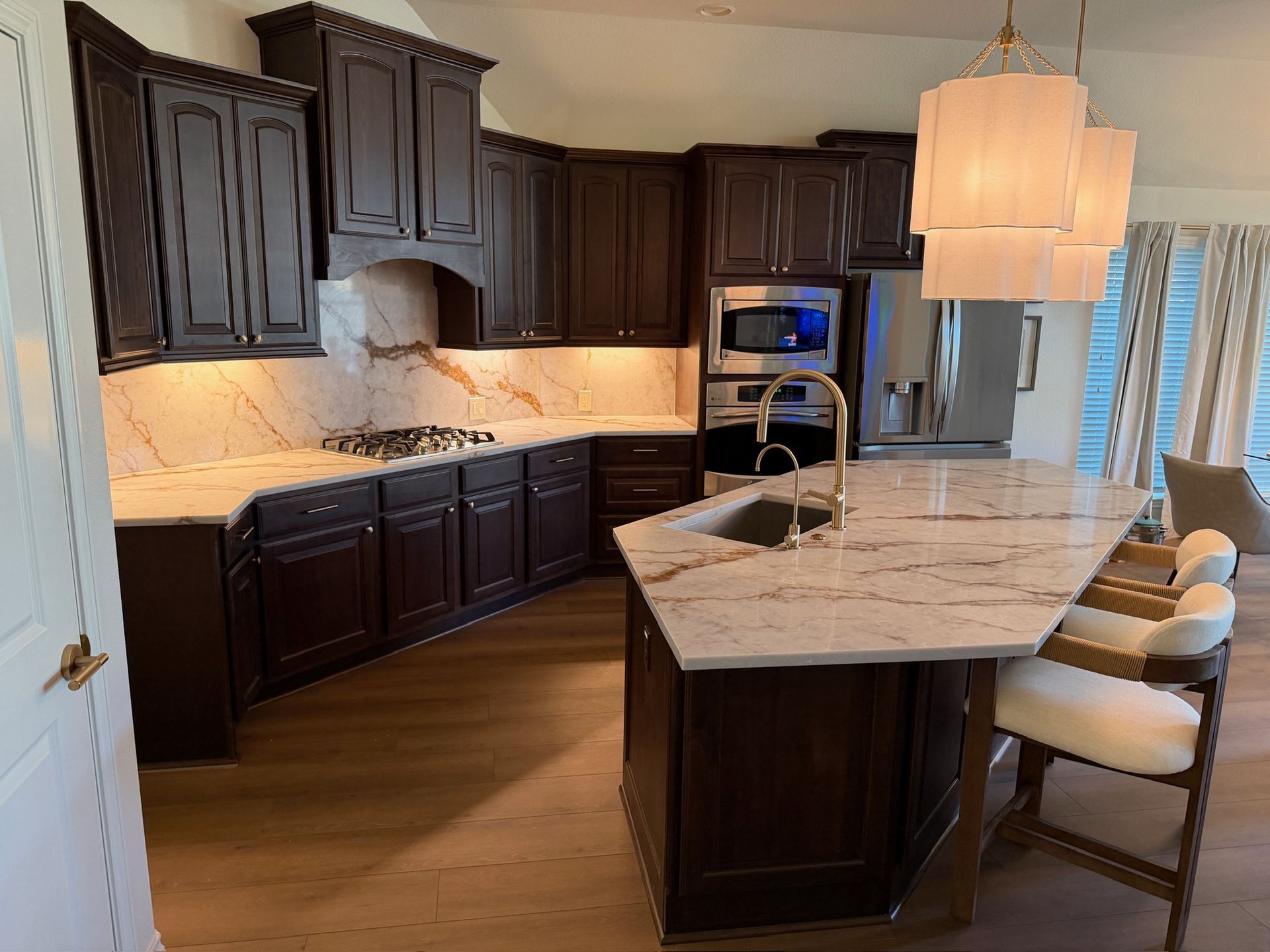 Teal kitchen with marble island, brass fixtures, and stainless steel appliances under pendant lights