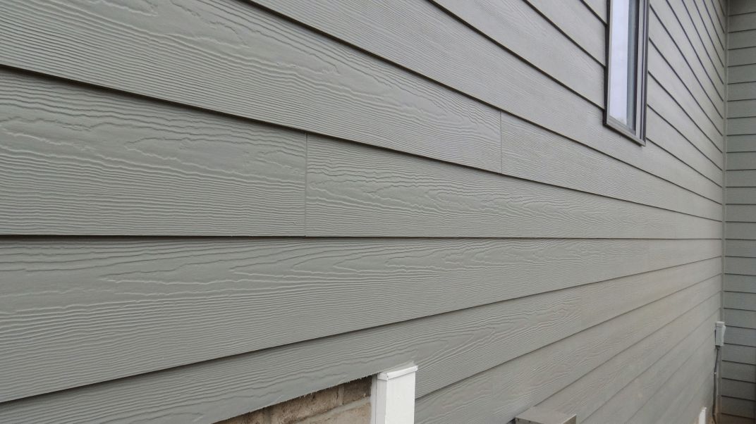 Gray vinyl siding on the side of a house with a small window and brown trim