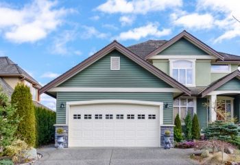 Suburban house with green siding and white garage under a blue sky