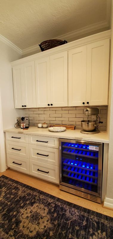 Built-in white cabinets and counter with undercounter blue-lit wine fridge in a kitchen nook