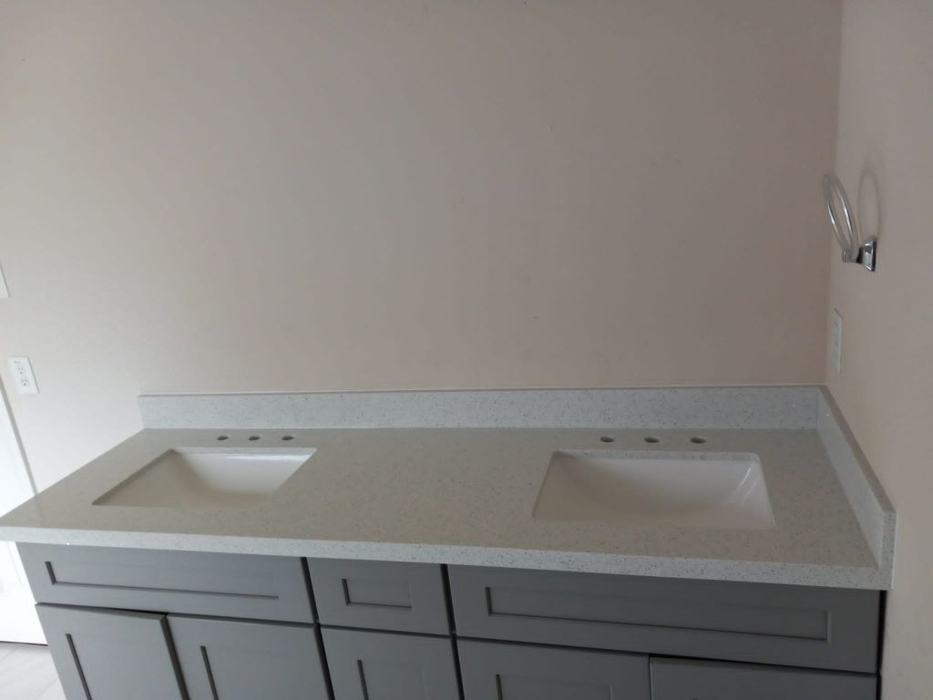 Bathroom vanity with two sinks and white countertop against a light wall, partially installed cabinets below