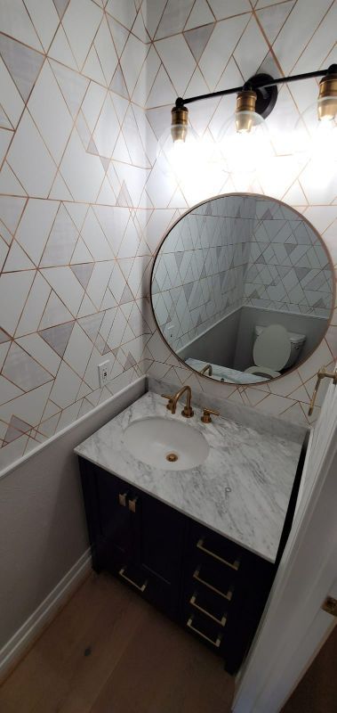 Narrow bathroom vanity with round mirror, marble countertop, dark cabinet, and diamond-pattern tiled walls.
