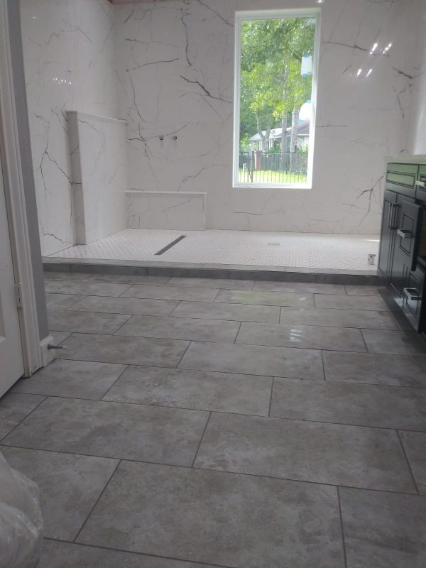 Modern bathroom with white marble walls, gray tile floor, walk-in shower, and window view outside