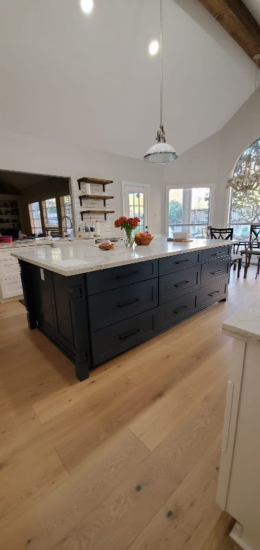 Bright kitchen with a large dark island, white counters, pendant lights, and wood floors
