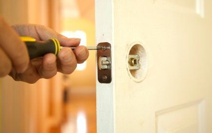 Hand using a screwdriver to install a door lock on a white door