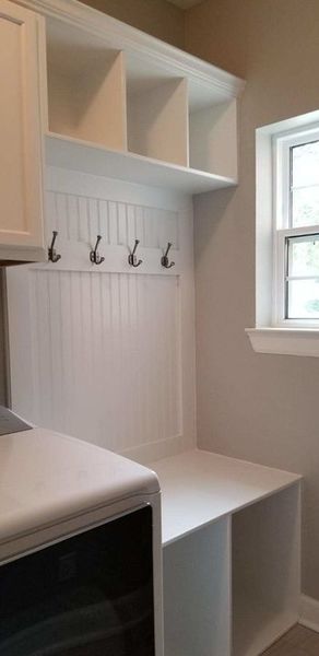 White mudroom nook with hooks, cubbies, bench, and a window.