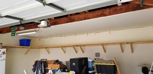 Garage interior with open door, wall shelves, and storage items along the back wall