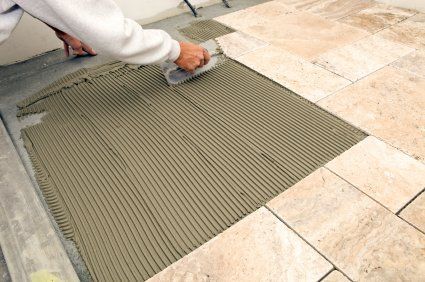 Person spreading mortar on a tiled floor with a trowel during tile installation