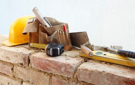 Construction tools and a yellow hard hat on a brick wall