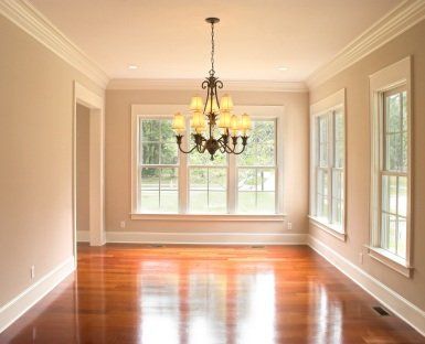 Empty beige dining room with hardwood floors, chandelier, and large windows overlooking greenery