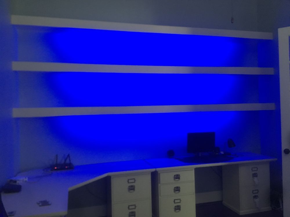 Blue-lit office desk with shelves and cabinets beneath a wall-mounted workspace