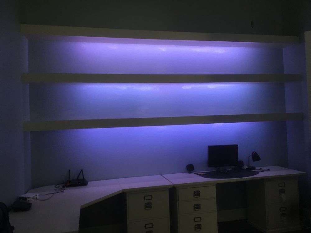 Empty office desk with two blue-lit shelves on the wall and a computer on the right