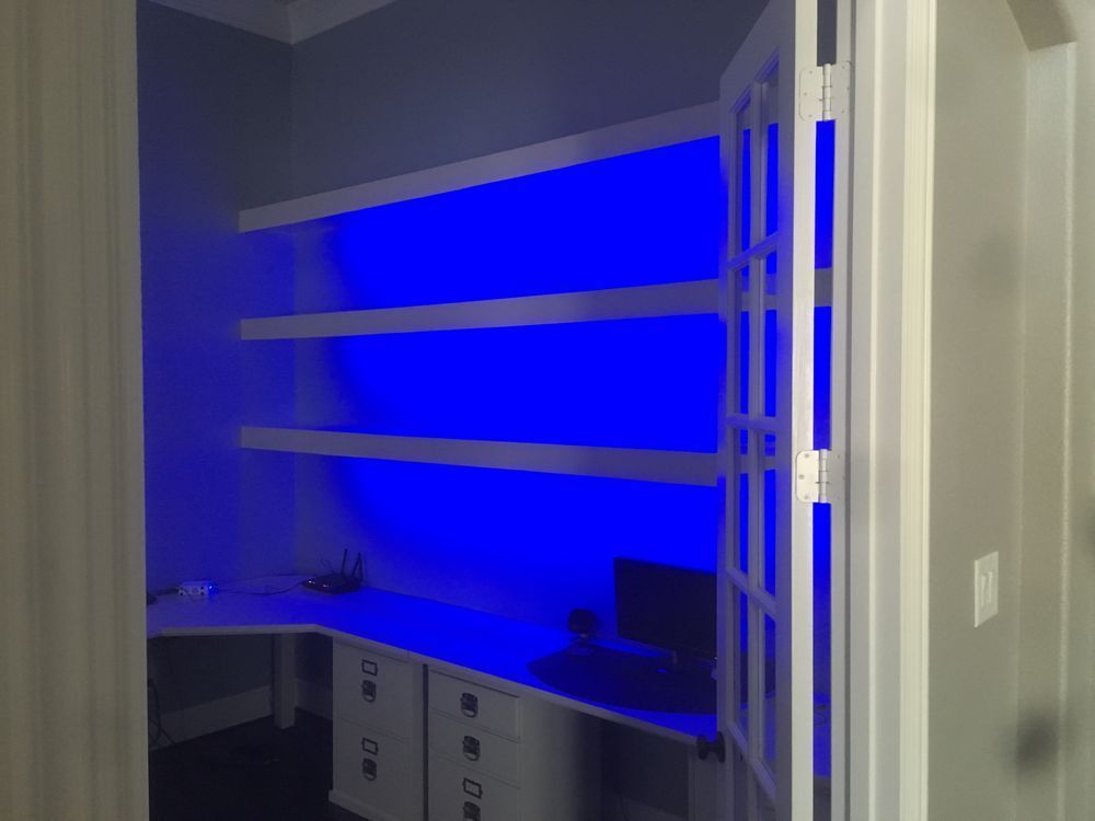 Blue-lit home office corner with shelves, desk, and cabinets built into a closet space