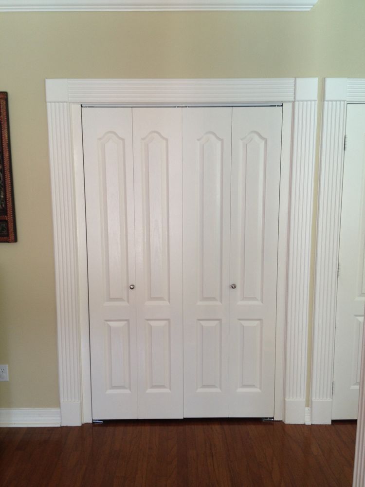 White double closet doors with ornate panels in a room with beige walls and hardwood floor