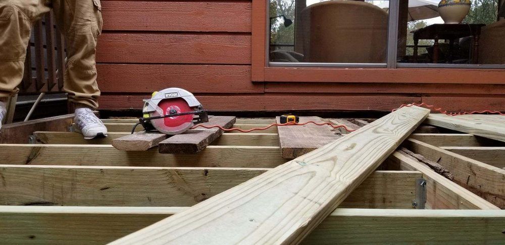 Circular saw on wooden deck framing beside a person’s boot and house siding