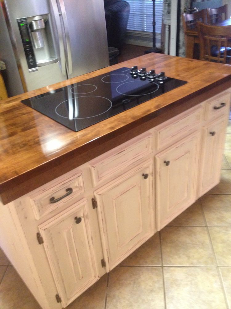 Kitchen island with built-in black cooktop and light wood cabinets on a tiled floor