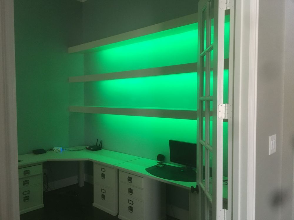 Modern office cubicle with glowing green backlit shelves and built-in desks