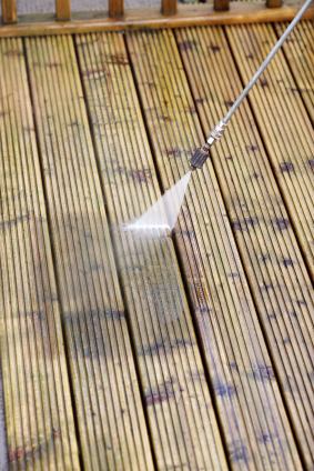 Person pressure-washing a wooden deck with a spray nozzle